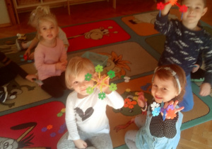 dzieci siedzą na dywanie i prezentują swoje budowle z klocków