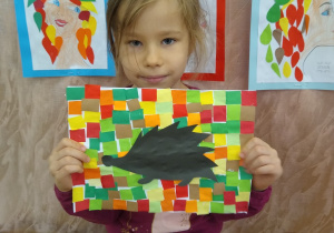 Dziewczynka prezentuje swoją pracę, czarny jeż na kolorowym tle