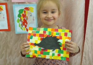 Dziewczynka prezentuje swoją pracę, czarny jeż na kolorowym tle