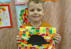 Chłopiec prezentuje swoją pracę, czarny jeż na kolorowym tle