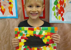 Chłopiec prezentuje swoją pracę, czarny jeż na kolorowym tle