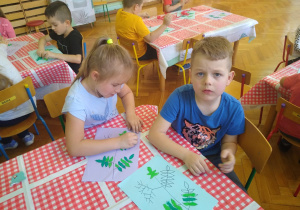 Dzieci wyklejają zielona plastelina i kulkami z czerwonej bibuły kontur gałązki jarzębiny