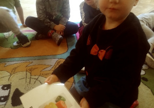 dzieci siedzą na dywanie i odkrywją kartki z warzywami