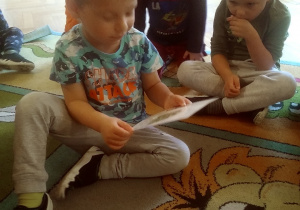 dzieci siedzą na dywanie i odkrywją kartki z warzywami