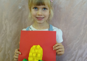 Dziewczynka prezentuje swoją pracę - kukurydza z zielonego i żółtego papieru na czerwonym tle