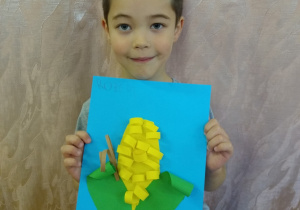 Chłopiec prezentuje swoją pracę - kukurydza z zielonego i żółtego papieru na niebieskim tle