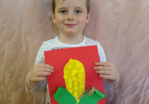 Chłopiec prezentuje swoją pracę - kukurydza z zielonego i żółtego papieru na czerwonym tle