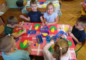 Dzieci przy stolikach naklejają kukurydzę z zielonego i żółtego papieru